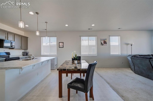 kitchen with sink, a kitchen breakfast bar, black appliances, light carpet, and decorative light fixtures