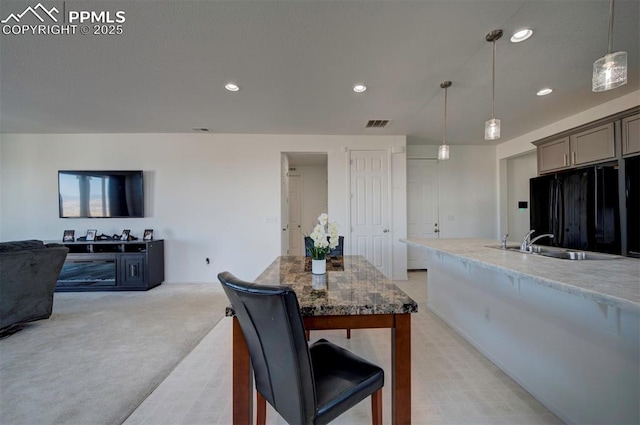 kitchen featuring hanging light fixtures, light colored carpet, sink, and black fridge