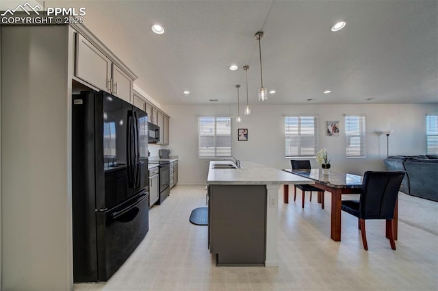 kitchen with sink, gray cabinetry, hanging light fixtures, a kitchen island with sink, and black appliances