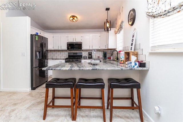 kitchen with decorative backsplash, appliances with stainless steel finishes, white cabinetry, a sink, and a peninsula