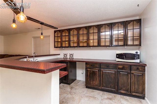 kitchen with decorative light fixtures, visible vents, dark brown cabinets, dark countertops, and glass insert cabinets