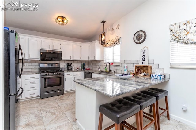 kitchen featuring appliances with stainless steel finishes, a peninsula, light stone countertops, a sink, and backsplash