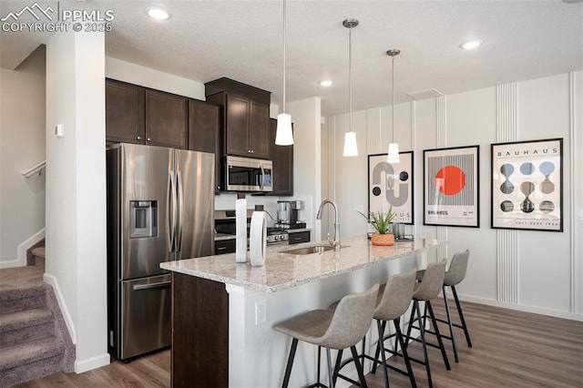 kitchen featuring a breakfast bar, sink, decorative light fixtures, an island with sink, and stainless steel appliances