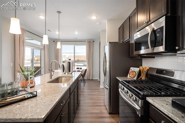 kitchen featuring sink, hanging light fixtures, light stone counters, stainless steel appliances, and a center island with sink