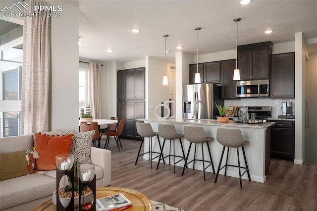 kitchen featuring appliances with stainless steel finishes, a kitchen island with sink, a kitchen bar, dark hardwood / wood-style flooring, and decorative light fixtures