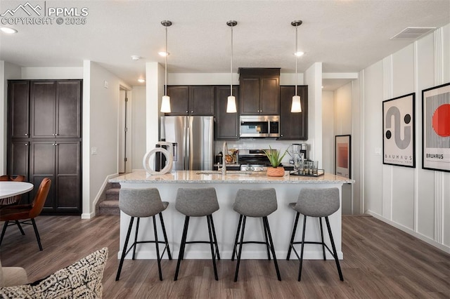 kitchen with appliances with stainless steel finishes, sink, hanging light fixtures, a kitchen island with sink, and dark brown cabinetry