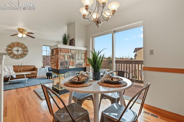 dining space featuring a stone fireplace, ceiling fan with notable chandelier, and light hardwood / wood-style floors