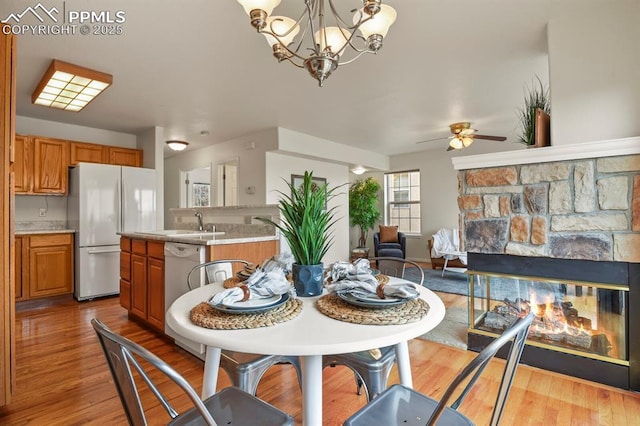 dining space with ceiling fan with notable chandelier, sink, a fireplace, and light hardwood / wood-style floors