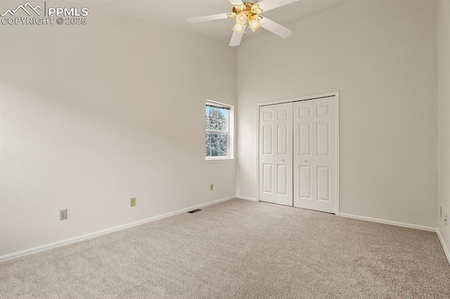 unfurnished bedroom featuring a towering ceiling, light colored carpet, a closet, and ceiling fan