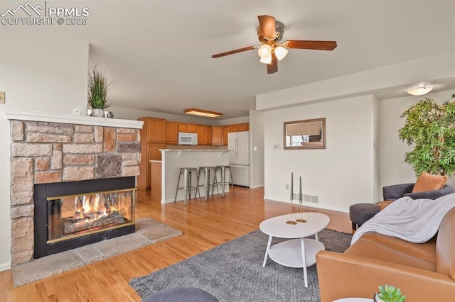 living room featuring a fireplace, light hardwood / wood-style flooring, and ceiling fan