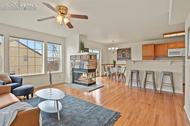 living room with a stone fireplace, ceiling fan with notable chandelier, and light hardwood / wood-style flooring