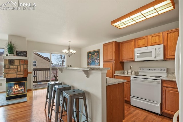 kitchen featuring light wood-type flooring, a kitchen bar, hanging light fixtures, a center island, and white appliances