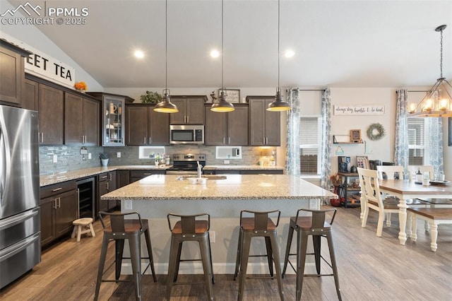 kitchen featuring dark brown cabinetry, light stone counters, an island with sink, pendant lighting, and stainless steel appliances