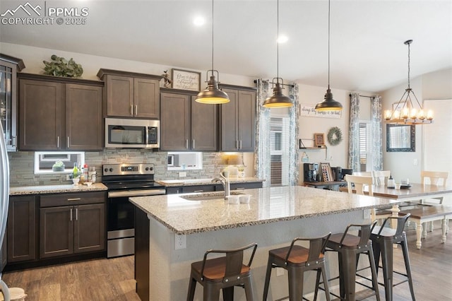 kitchen with hanging light fixtures, a center island with sink, appliances with stainless steel finishes, a kitchen breakfast bar, and light stone countertops