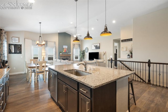 kitchen featuring dark brown cabinets, sink, light stone counters, and decorative light fixtures