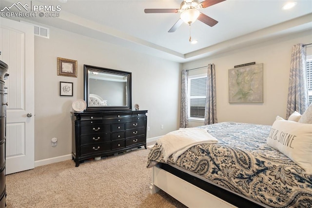 bedroom with light colored carpet, a raised ceiling, and ceiling fan