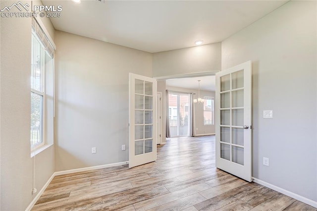 unfurnished room featuring light hardwood / wood-style flooring, an inviting chandelier, and french doors