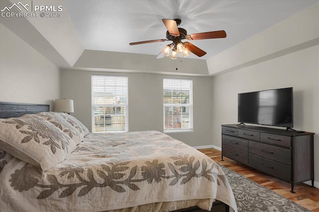 bedroom featuring ceiling fan, a raised ceiling, and light hardwood / wood-style flooring