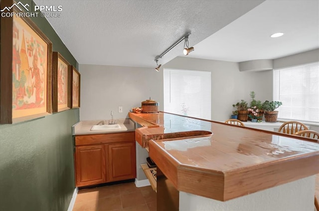 kitchen with light tile patterned flooring, rail lighting, sink, and a textured ceiling