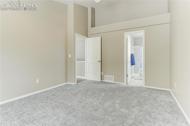 unfurnished bedroom featuring connected bathroom, a towering ceiling, and light colored carpet