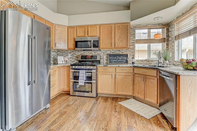 kitchen featuring sink, tasteful backsplash, hanging light fixtures, light wood-type flooring, and appliances with stainless steel finishes