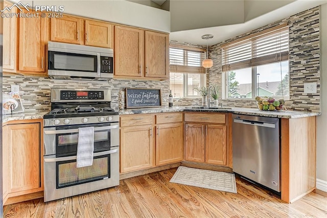 kitchen with sink, tasteful backsplash, light wood-type flooring, appliances with stainless steel finishes, and light stone countertops