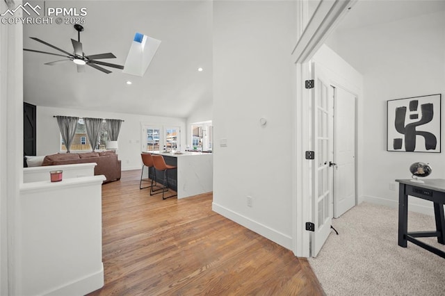 home office featuring ceiling fan, a skylight, high vaulted ceiling, and light hardwood / wood-style flooring