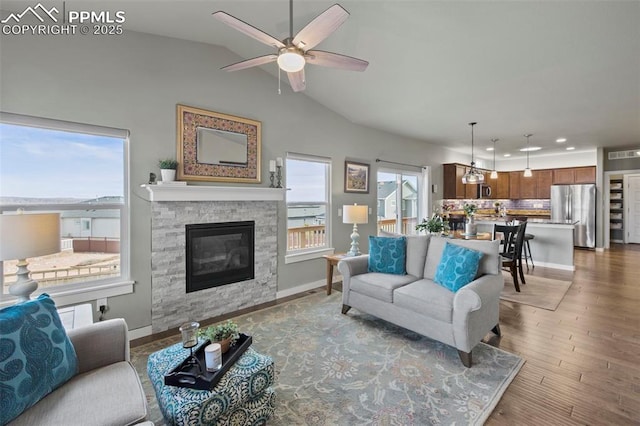 living room featuring visible vents, ceiling fan, a stone fireplace, wood finished floors, and baseboards