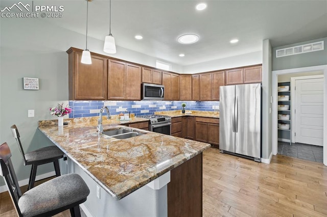 kitchen with light stone counters, a peninsula, a sink, visible vents, and appliances with stainless steel finishes