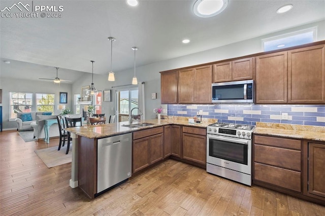 kitchen featuring tasteful backsplash, light wood-style flooring, appliances with stainless steel finishes, a peninsula, and a sink