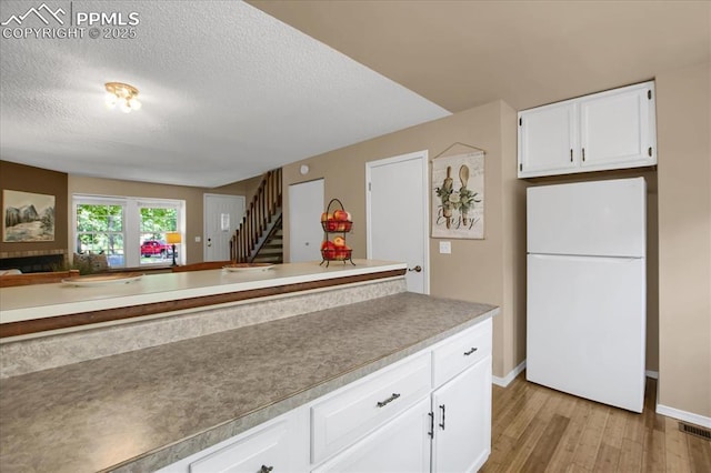 kitchen with light hardwood / wood-style flooring, a textured ceiling, white fridge, and white cabinets