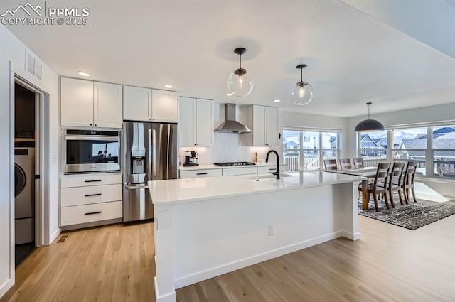 kitchen with pendant lighting, sink, appliances with stainless steel finishes, white cabinetry, and wall chimney exhaust hood