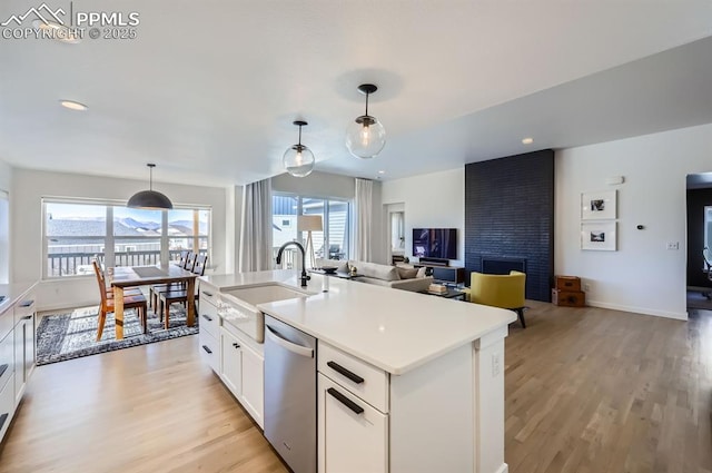 kitchen featuring sink, white cabinetry, hanging light fixtures, dishwasher, and an island with sink