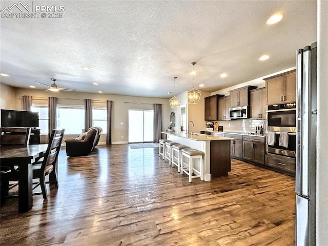 kitchen with a kitchen bar, hanging light fixtures, appliances with stainless steel finishes, dark hardwood / wood-style flooring, and a kitchen island with sink