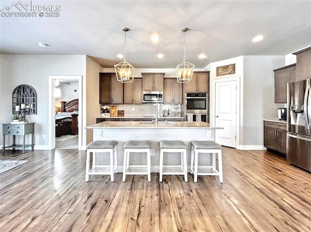 kitchen with a breakfast bar area, hanging light fixtures, stainless steel appliances, a center island with sink, and light hardwood / wood-style flooring