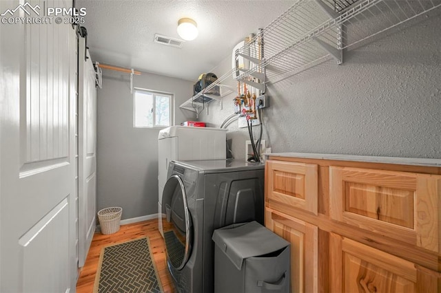 laundry area with a textured ceiling, independent washer and dryer, and light hardwood / wood-style flooring