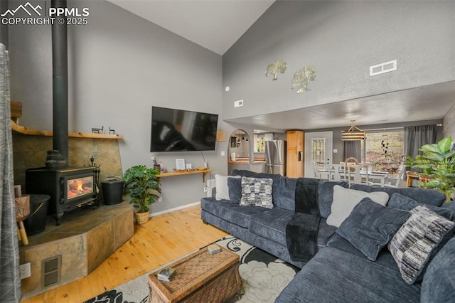 living room with a healthy amount of sunlight, high vaulted ceiling, hardwood / wood-style floors, and a wood stove