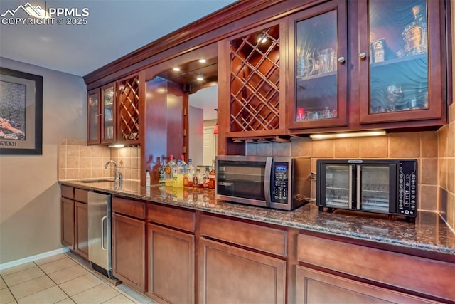 bar featuring backsplash, dark stone counters, sink, and light tile patterned floors