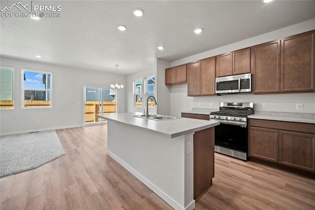 kitchen with sink, appliances with stainless steel finishes, an island with sink, decorative light fixtures, and light wood-type flooring