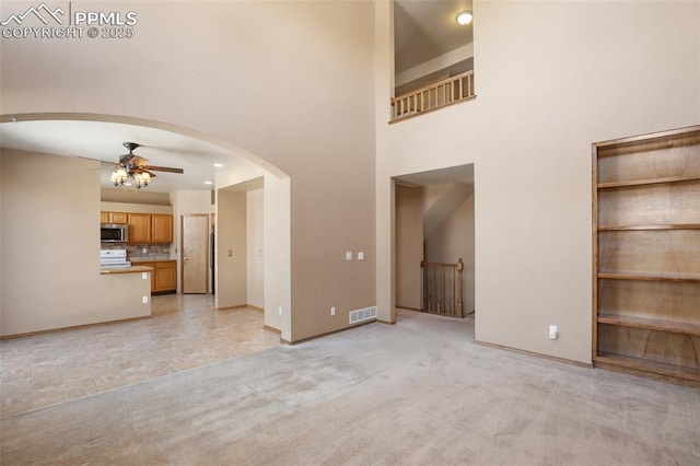 unfurnished living room with ceiling fan, light colored carpet, and a towering ceiling