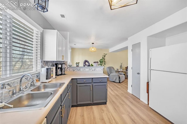 kitchen featuring gray cabinets, sink, white refrigerator, hanging light fixtures, and kitchen peninsula