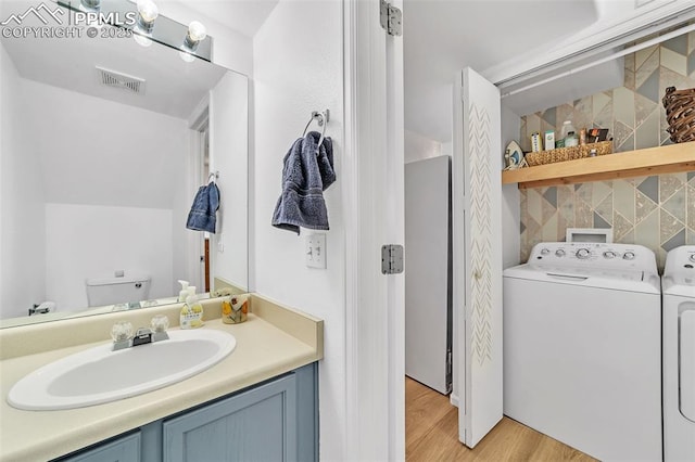 bathroom with wood-type flooring, toilet, washer and dryer, and vanity