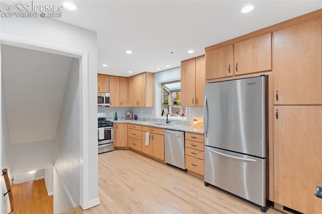 kitchen featuring light brown cabinetry, light stone countertops, stainless steel appliances, and light wood-type flooring