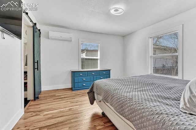 bedroom featuring a textured ceiling, a barn door, light wood-style flooring, baseboards, and a wall mounted AC