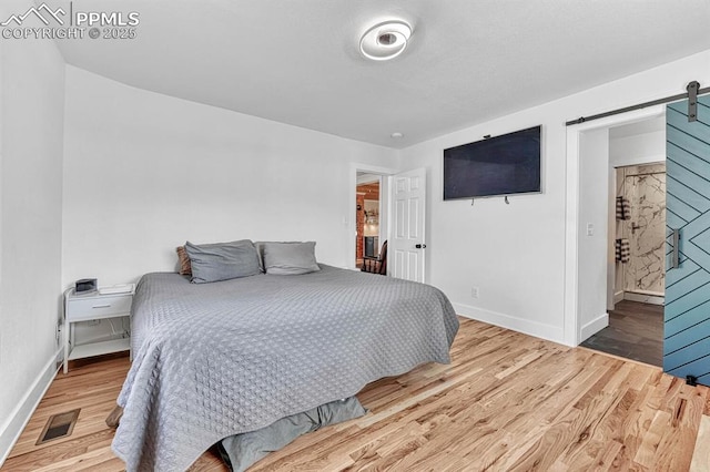 bedroom featuring a barn door, wood finished floors, visible vents, and baseboards