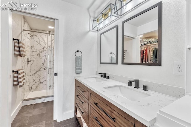 bathroom with a sink, a spacious closet, a marble finish shower, and double vanity