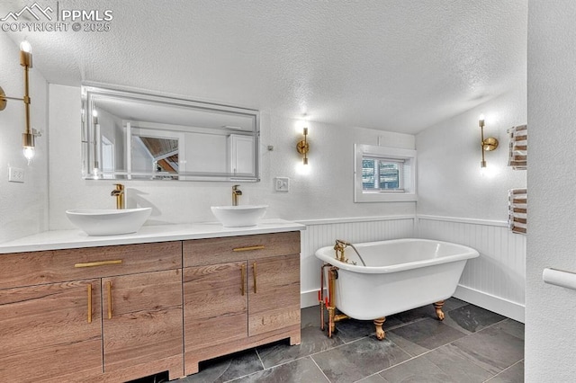 bathroom featuring a wainscoted wall, a sink, a textured ceiling, and double vanity