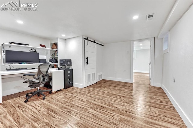 unfurnished office with light wood-style floors, a barn door, visible vents, and baseboards