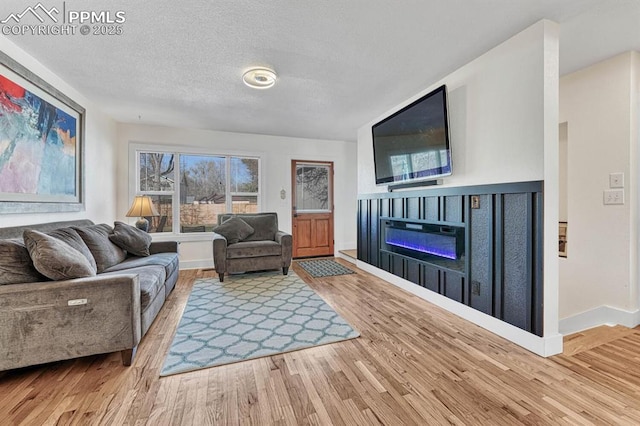 living room with a textured ceiling, a glass covered fireplace, wood finished floors, and baseboards