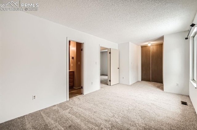 unfurnished bedroom featuring ensuite bathroom, light colored carpet, a textured ceiling, and a closet